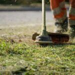 Close-up of a person trimming grass with a power tool outdoors.